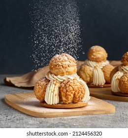 Delicious cakes profiterole choux pastry with custard and powder on a gray concrete background. Craquelin Choux biscuits.