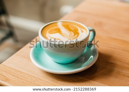 Delicious cappuccino with beautiful foam in a blue ceramic mug on a wooden table. Freshly brewed coffee with beautiful latte art in a light coffee shop