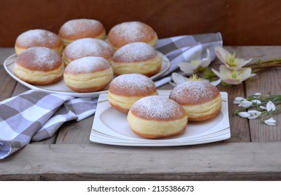 Delicious carnival donuts. Home baked berliner donuts with snowdrops and hellebores on wood covered with dishcloth. Doughnuts made of rich sweet dough, stuffed with jam, sprinkled with sugar powder. 