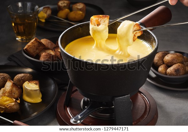 Delicious cheese fondue\
with dipping forks coated in melted cheese surrounded by assorted\
breads and potatoes