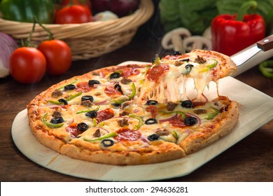 Delicious cheese stringy slice lifted of full supreme pizza baked fresh out of the oven next to ingredients - Powered by Shutterstock