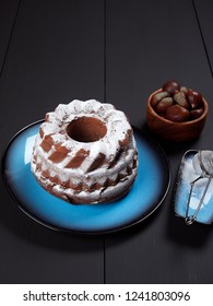 Delicious Chestnut Bundt Cake Using Sweetened Chestnut Purée And Chocolate Chips, Dusted With Sugar, Set On A Blue Plate, On A Dark Brown Background    