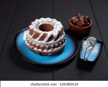 Delicious Chestnut Bundt Cake Using Sweetened Chestnut Purée And Chocolate Chips, Dusted With Sugar, Set On A Blue Plate, On A Dark Brown Background    