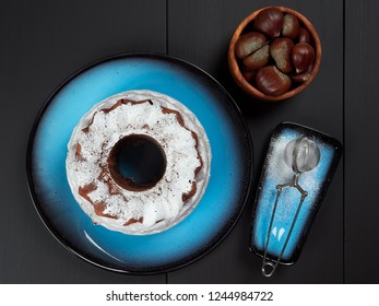 Delicious Chestnut Bundt Cake Using Sweetened Chestnut Purée And Chocolate Chips, Dusted With Sugar, Set On A Blue Plate, On A Dark Brown Background    