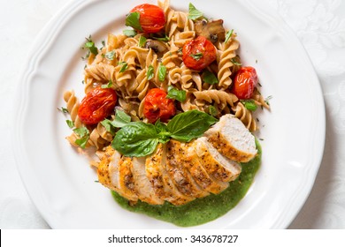 A Delicious Chicken And Whole Grain Pasta Dinner On A White Plate With Fresh Basil. Shot From Overhead View.