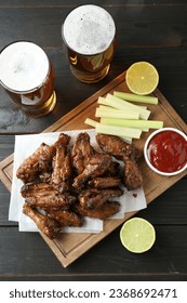 Delicious chicken wings served with beer on black wooden table, flat lay - Shutterstock ID 2368692471