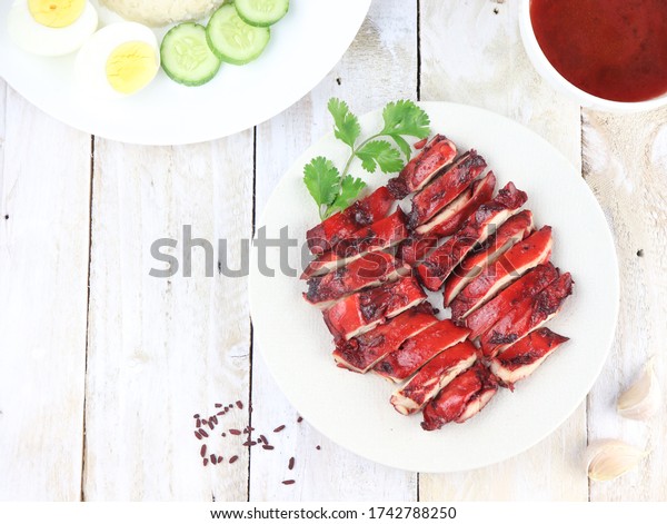 Delicious Chinese Cuisine Ayam Char Siu or Grilled\
Char Siu Chicken or Char Siew, vibrant red chicken made from angkak\
or red yeast rice. Served in white plate on wooden table. Selective\
focus.