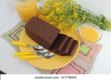 Delicious chocolate cake on yellow plate, orange marmalade on light background and flowers