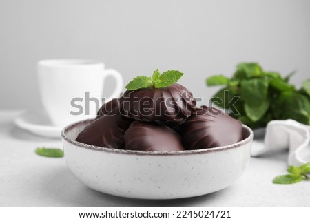 Delicious chocolate covered zephyrs with mint in bowl on white table