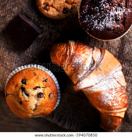 Delicious Chocolate cupcakes, croissants and dark chocolate pieces on wooden table  - Food background, bakery concept, close up image