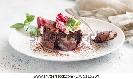 Delicious chocolate fondant or lava cake with cream, raspberries and mint, light grey concrete background. Hot chocolate dessert (pudding) with liquid center. Fondant au chocolate. 