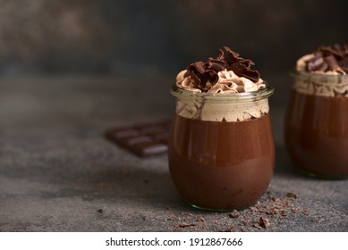 Delicious chocolate mousse or pudding with whipped cream in a vintage glass jar on a dark slate, stone or concrete background.