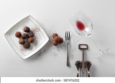 Delicious chocolate truffles and empty wine glass on white table