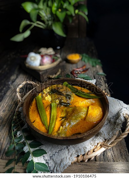 Delicious coconut milk fish curry\
with lady fingers on a wooden bowl over dark background.\
\
