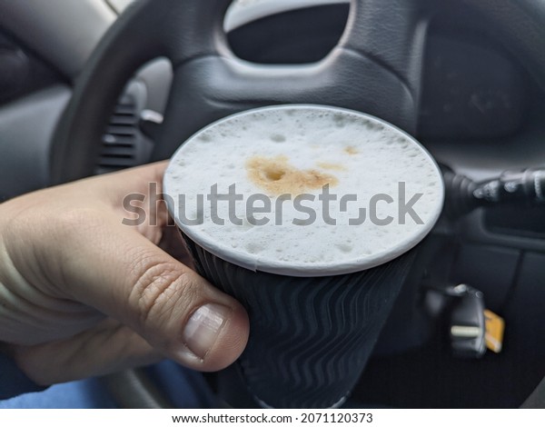 delicious coffee with froth in the car. the\
driver of the car drinks coffee. travel coffee. milkshake in the\
car salon. cappuccino with foam in a glass\
