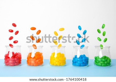Delicious color jelly beans falling into jars on light blue table