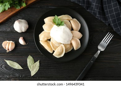 Delicious cooked dumplings with sour cream on dark wooden table, flat lay