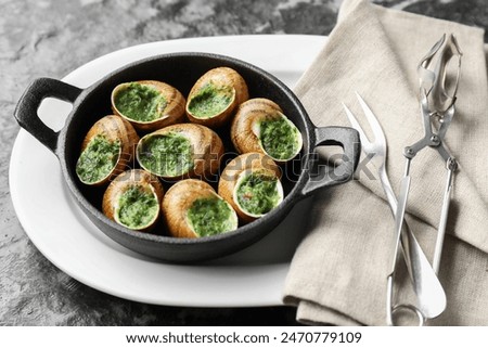 Delicious cooked snails in baking dish served on grey textured table