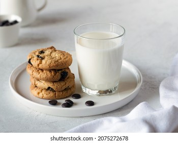 Delicious cookies with chocolate on a white plate and fresh milk in a glass on a light table. An idea for a children's breakfast or snack. Selective focus