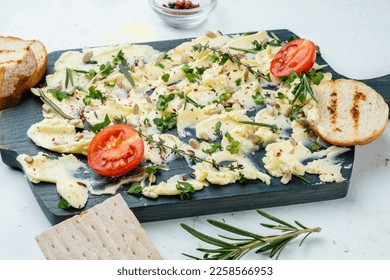 Delicious creamy butter snack with herbs and seeds, served on a wooden board with baguette and crackers, light background. - Shutterstock ID 2258566953