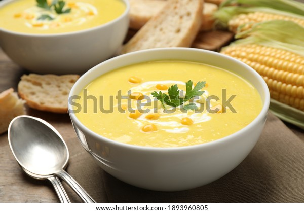 Delicious creamy corn soup served on wooden\
table, closeup