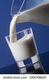 Délicieux lait frais crémeux versé de la carafe dans un verre et isolé sur fond bleu