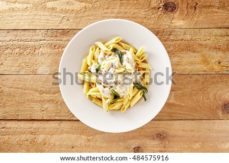 Delicious creamy Italian penne pasta starter with pepper seasoning and fresh basil viewed from above on rustic wooden centered with copy space