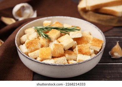 Delicious crispy croutons with rosemary in bowl on wooden table, closeup