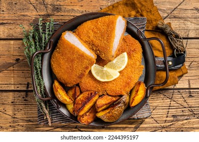 Delicious crispy pork schnitzel with fried potato wedges. Wooden background. Top view.