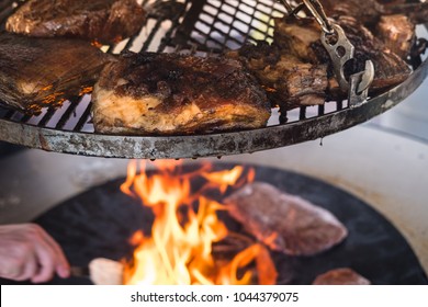 Delicious Crusty Pork Roast On A Bbq Grill, The Grillmaster Is Taking Care Of The Charcoal Fire Underneath