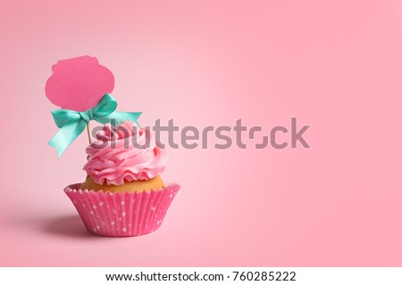 Delicious cupcake with greeting card on pink background