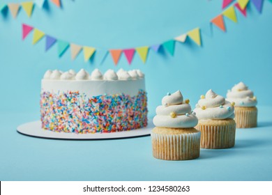 Delicious cupcakes and cake with sugar sprinkles on blue background with bunting