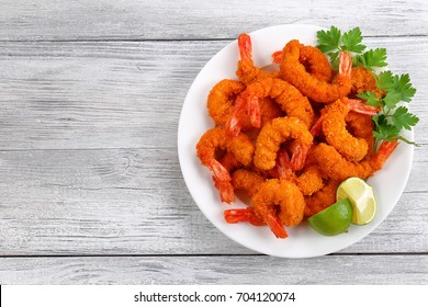 delicious deep fried breaded cheese prawn tails served with lime wedges and coriander leaves on white plate on wooden table, blank space for text left, view from above
