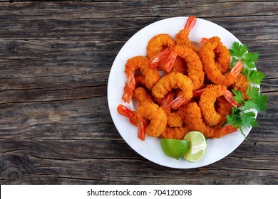 delicious deep fried breaded shrimps served with lime wedges and coriander leaves on white plate on wooden table, copy space for text, view from above
