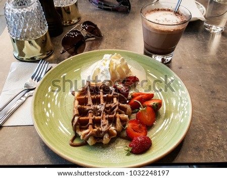Delicious dessert with waffles, strawberries, cream and hot chocolate with sunglasses. fork and knife summer