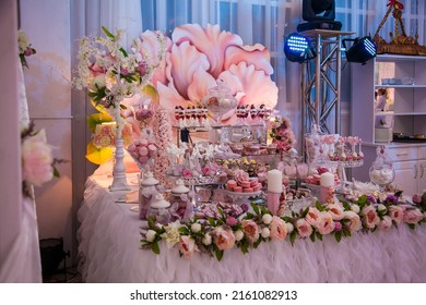 Delicious desserts at the wedding candy bar in the buffet area in neon light: decorated candles, rosebuds, ribbons, macaroons, strawberries in white chocolate.