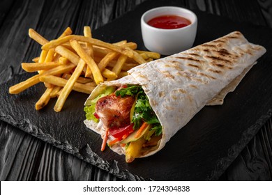 A delicious doner donair kebab wrap with meat, lettuce, tomato, red onion and sauce with french fries and sauce.