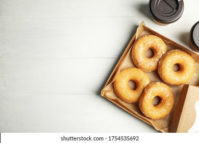 Delicious Donuts In Box And Coffee On White Table, Flat Lay. Space For Text