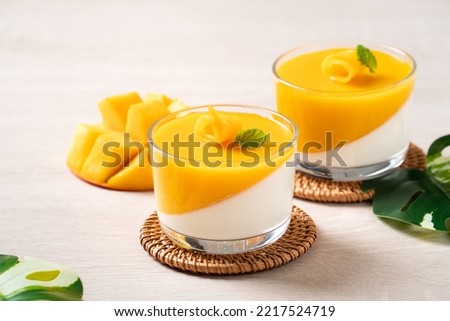 Delicious double colored mango panna cotta mousse pudding with diced mango pulp flesh topping on wooden table background.
