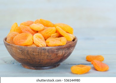Delicious dried apricots in wooden bowl over blue background