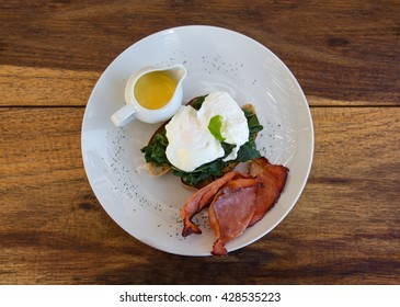 Delicious Eggs Benedict With Bacon And Spinach, Shot From Above On A Wooden Background