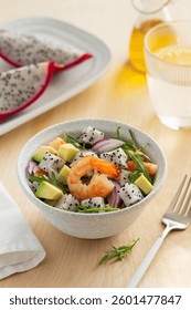 Deliciosa ensalada exótica con pitahaya, aguacate, camarones, rúcula y cebolla roja en un bol sobre mesa de madera.  Dieta saludable y alimentos bajos en calorías. Enfoque selectivo