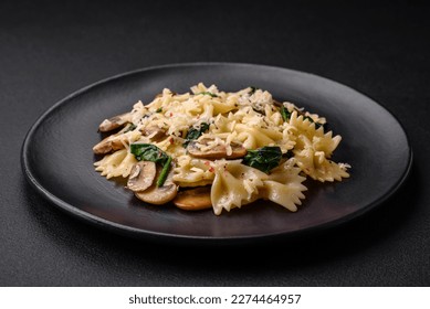 Delicious farfalle pasta with mushrooms, cheese and spinach with spices on a black plate on a dark concrete background - Powered by Shutterstock