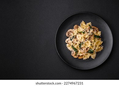 Delicious farfalle pasta with mushrooms, cheese and spinach with spices on a black plate on a dark concrete background - Powered by Shutterstock