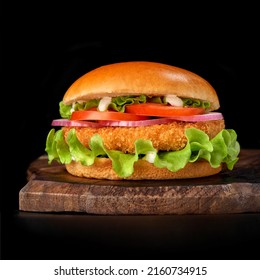 Delicious Fast Food Fresh Tasty Burger. Crispy, Breaded Chicken Burger With And Vegetable On Wooden Cutting Board, Isolated On Dark Background