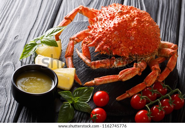Delicious food: boiled spider crab with tomato,\
lemon and melted butter close-up on a black board. Horizontal.\
restaurant setting\
