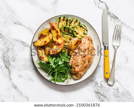 Delicious food - roasted potatoes, chicken breast, grilled zucchini and arugula spinach salad on a dark background, top view        