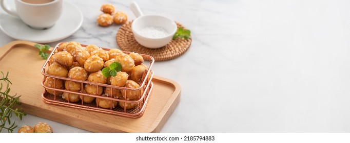 Delicious French Chouquette Choux Pastry dessert Pearl Sugar Puff in a basket on white marble background with a cup of milk tea, afternoon tea concept.