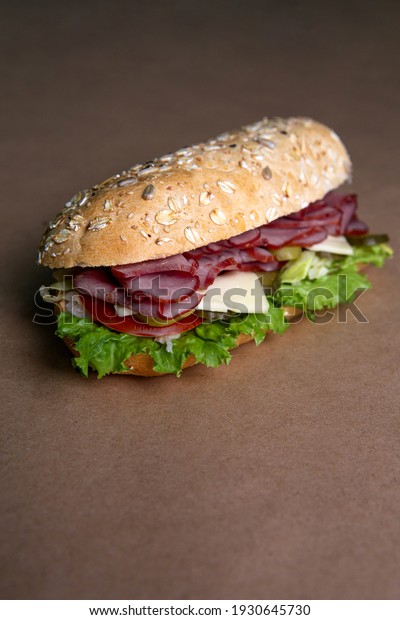Delicious fresh baguette sandwich\
with baked ham, cucumber, cheese and salad on ocher\
background