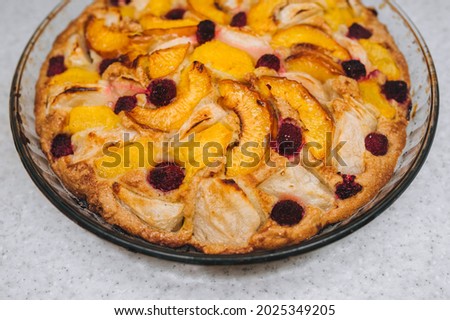 Delicious, fresh, baked apple, peach, raspberry pie close-up in a round glass form.